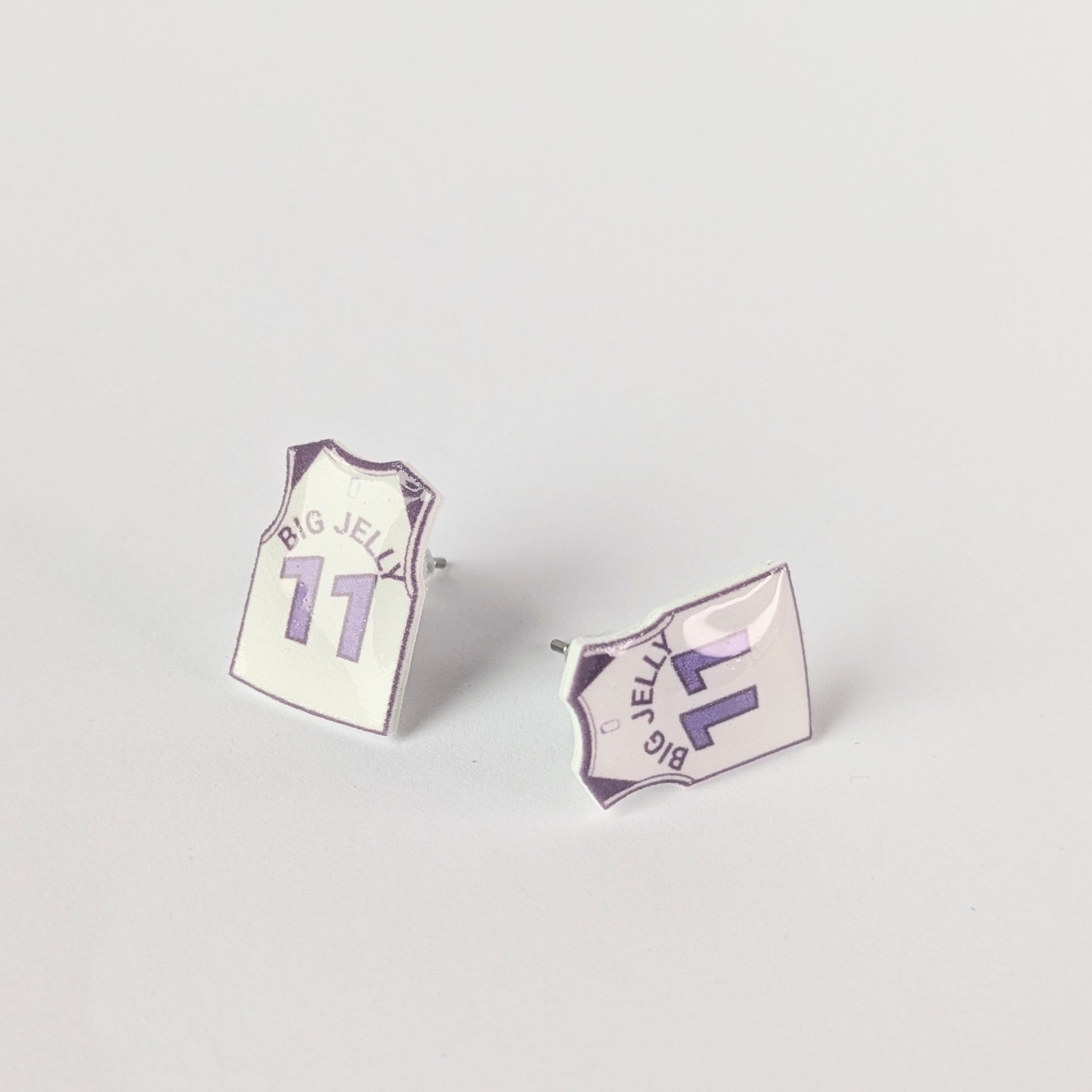 Two earrings shaped like miniature sports jerseys on a light gray background