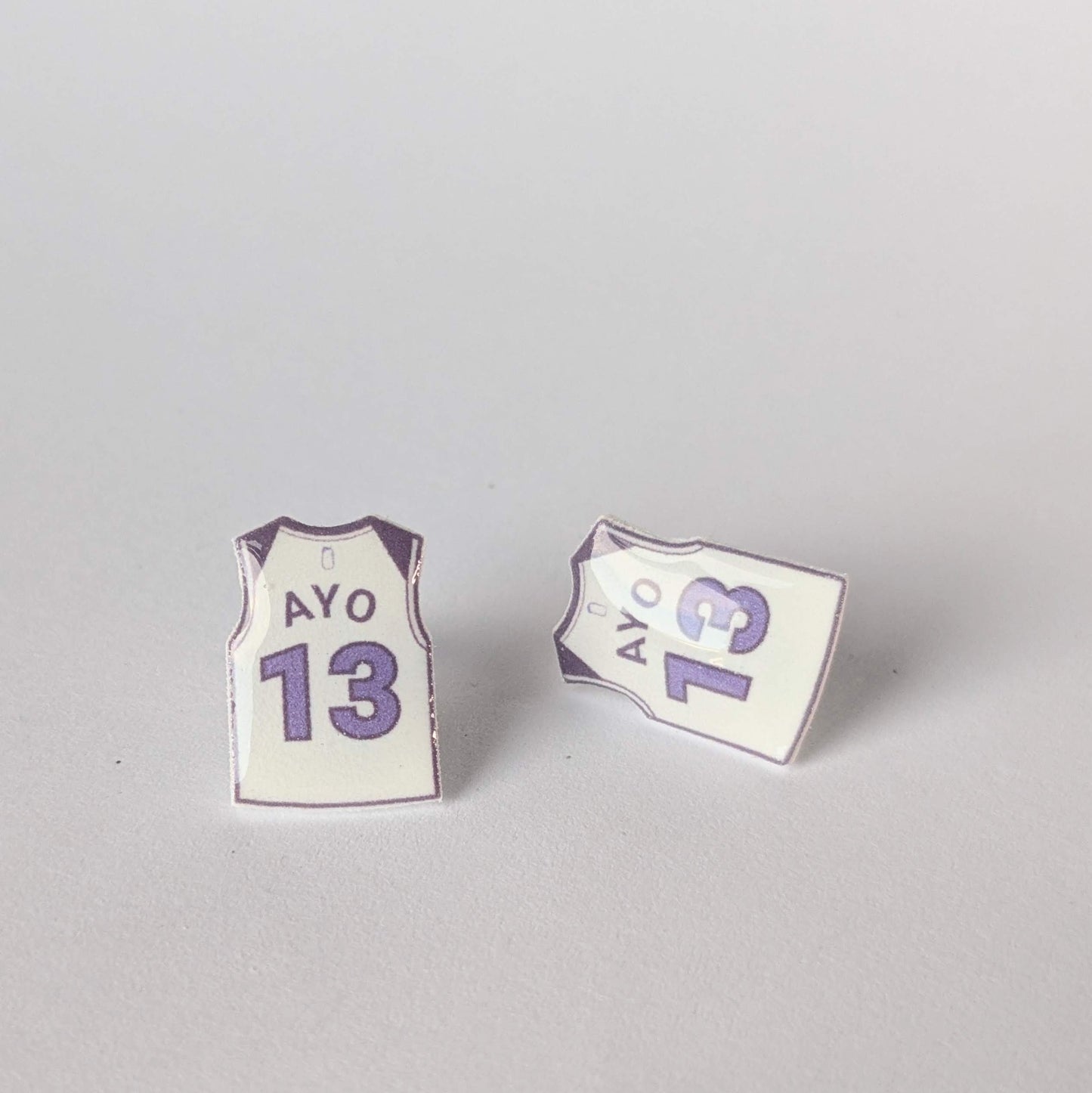 Two earrings shaped like basketball jerseys with 'AYO' and number '13' on a gray background