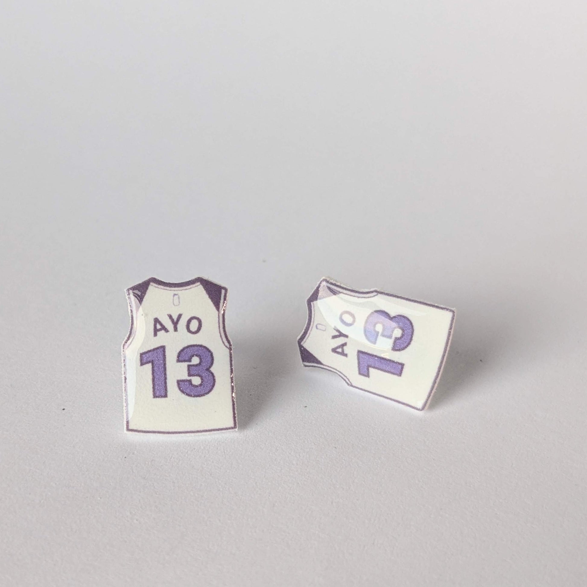 Two earrings shaped like basketball jerseys with 'AYO' and number '13' on a gray background