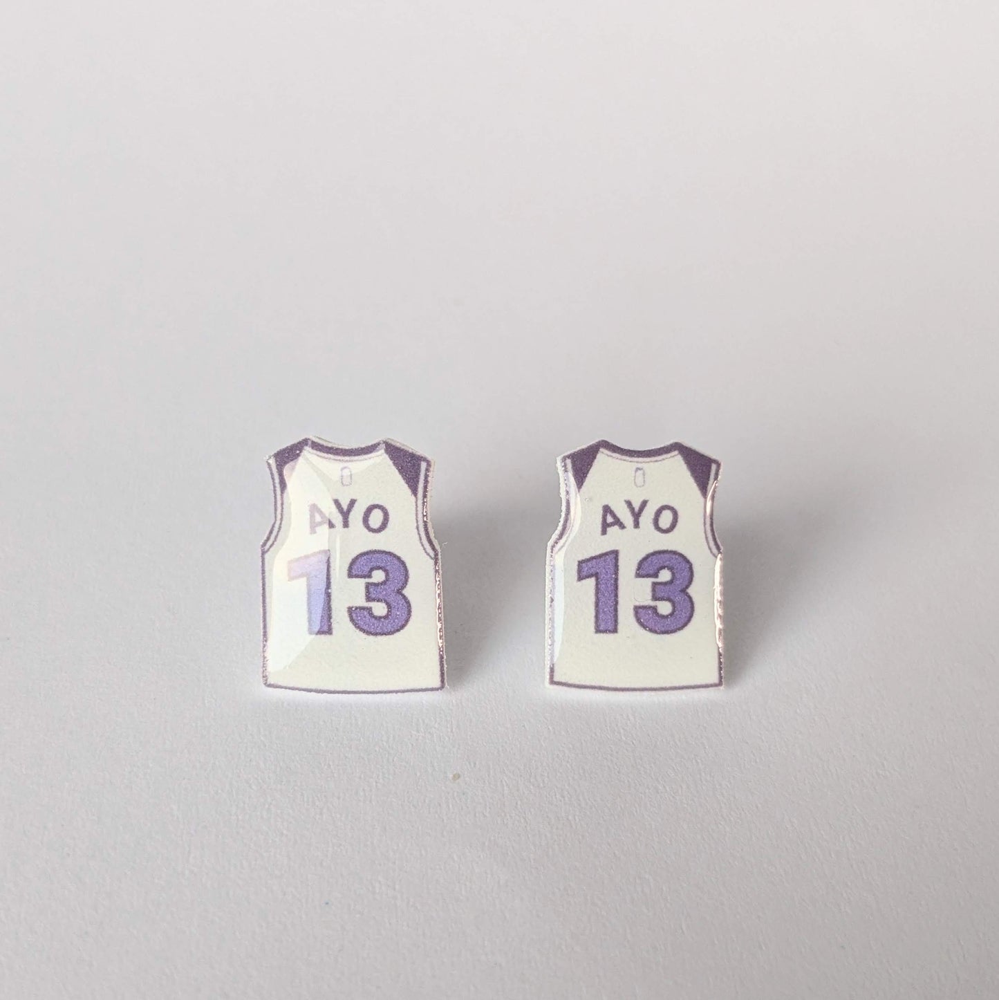 Two small earrings shaped like miniature basketball jerseys with 'AYO' and number '13' on a light gray background.