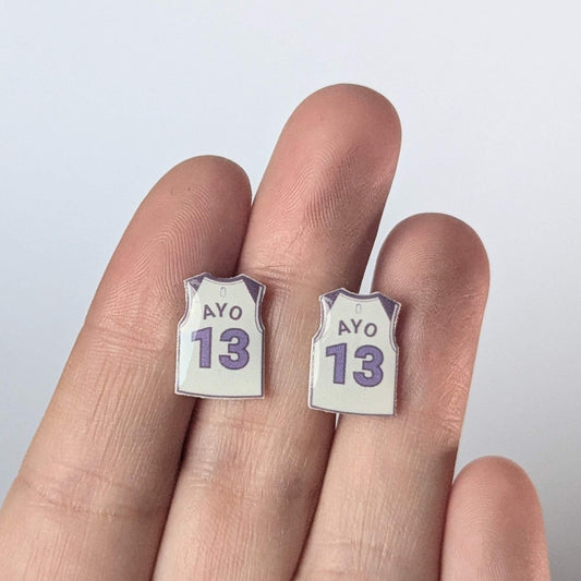 Earrings shaped like miniature basketball jerseys with the number 13 on a hand against a light background