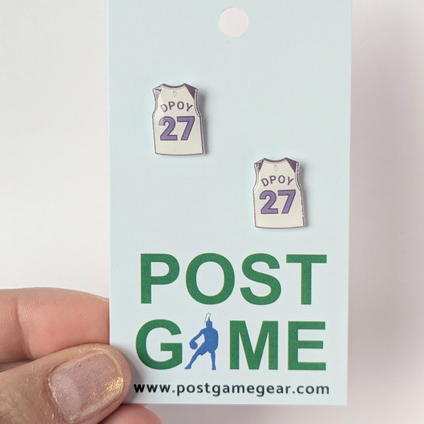 Two small earrings resembling basketball jerseys on a 'POST GAME' card with branding.