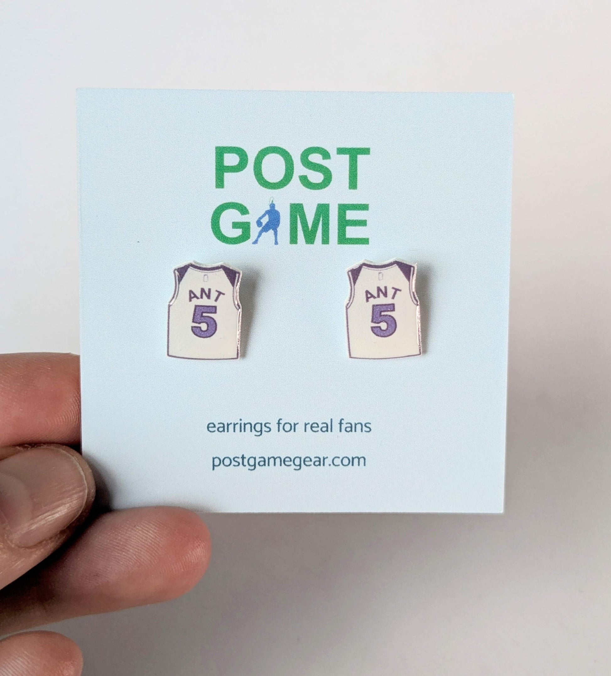 Basketball jersey earrings on a 'POST GAME' card held by a hand.