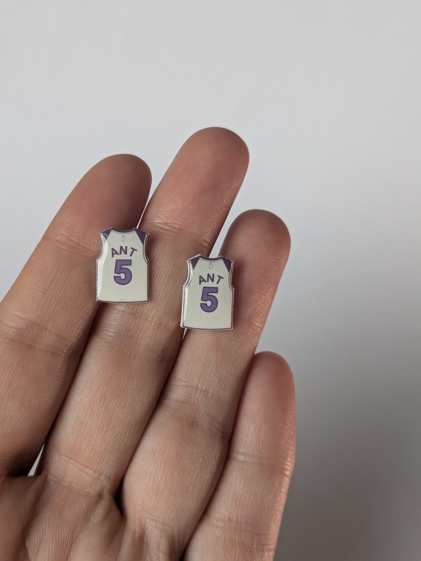 Pair of earrings shaped like basketball jerseys on a hand against a white background