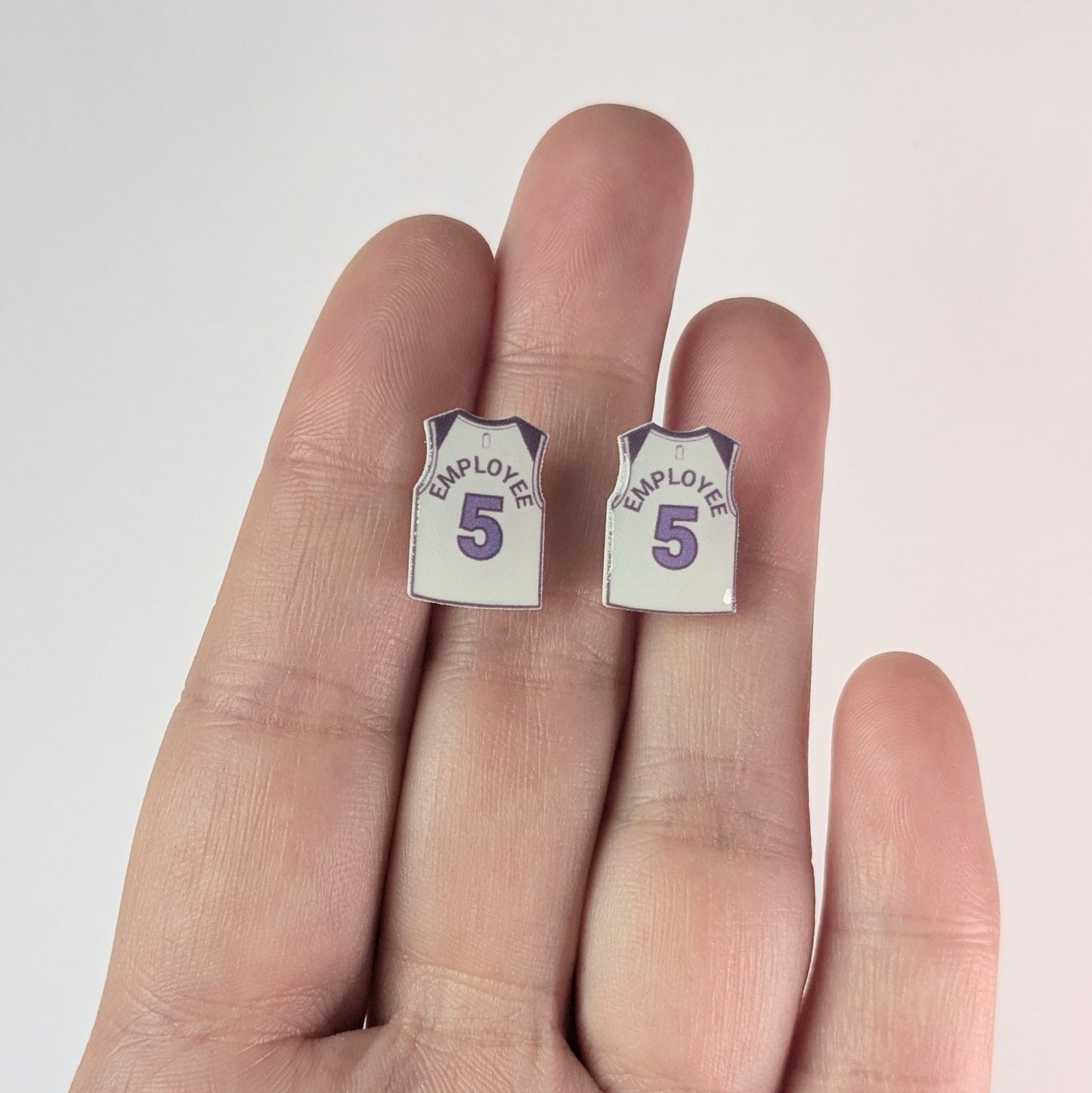 Pair of 'Employee 5' earrings held between fingers on a light background