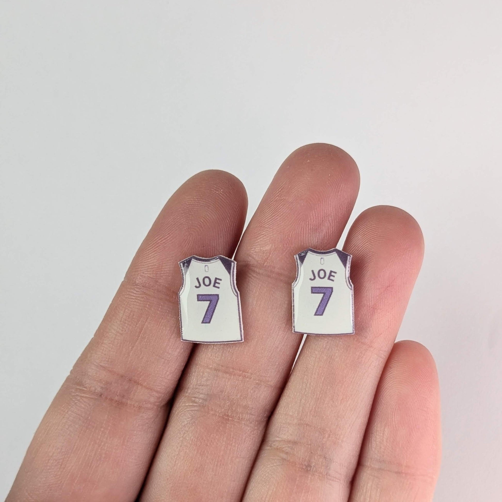 Pair of earrings shaped like miniature sports jerseys with 'JOE' and number '7' on a white background.